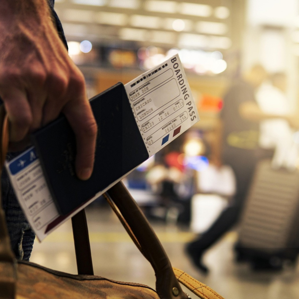 Close-up of a passenger holding a boarding pass and passport, preparing for departure inside a busy airport terminal.